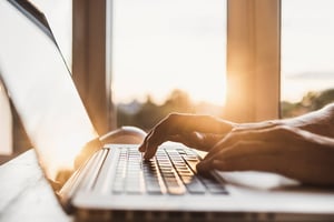 close up of hands on a laptop with sunset coming in through a window