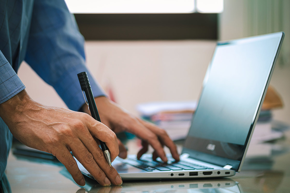 person typing on laptop with pen in hand close-up